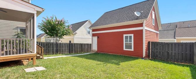 backyard with red shed and wooden fence. Green grassy backyard with clear blue skies.